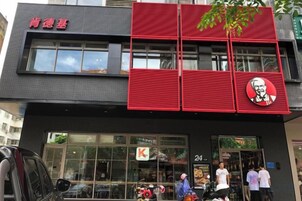 Un edificio con fachada roja y negra, un letrero de KFC y una entrada visible con gente afuera.