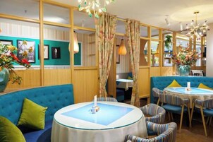 A restaurant with round tables, blue upholstered seating, and a decorative vase with flowers.