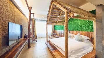 Quarto com cama, televisão, um banco de madeira e parede verde.