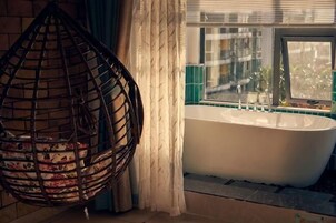 Un baño con bañera, una silla colgante y una ventana con cortinas.