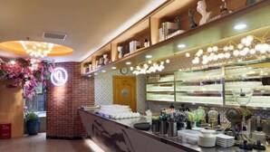 Zona bar ben illuminata, con un bancone, scaffali con oggetti decorativi e una sveglia appesa al muro.