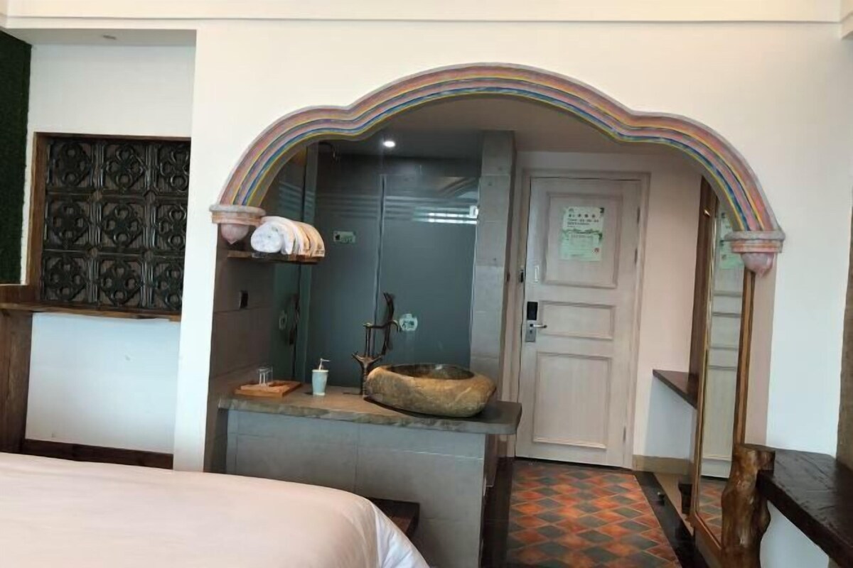 A room with a bed, a small sink with a stone basin, a mirror, and a decorative archway.