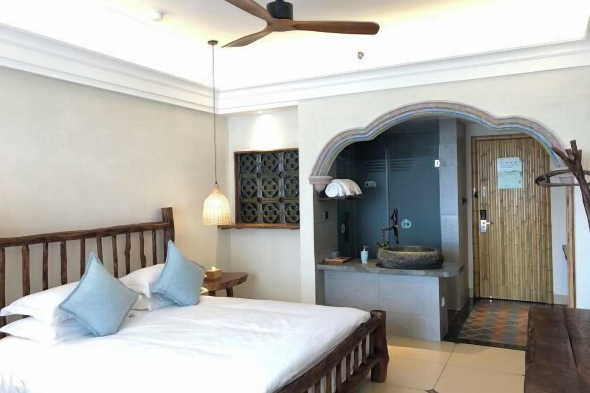 A bedroom with a wooden bed, a ceiling fan, a nightstand, and a bathroom with a sink and mirror.