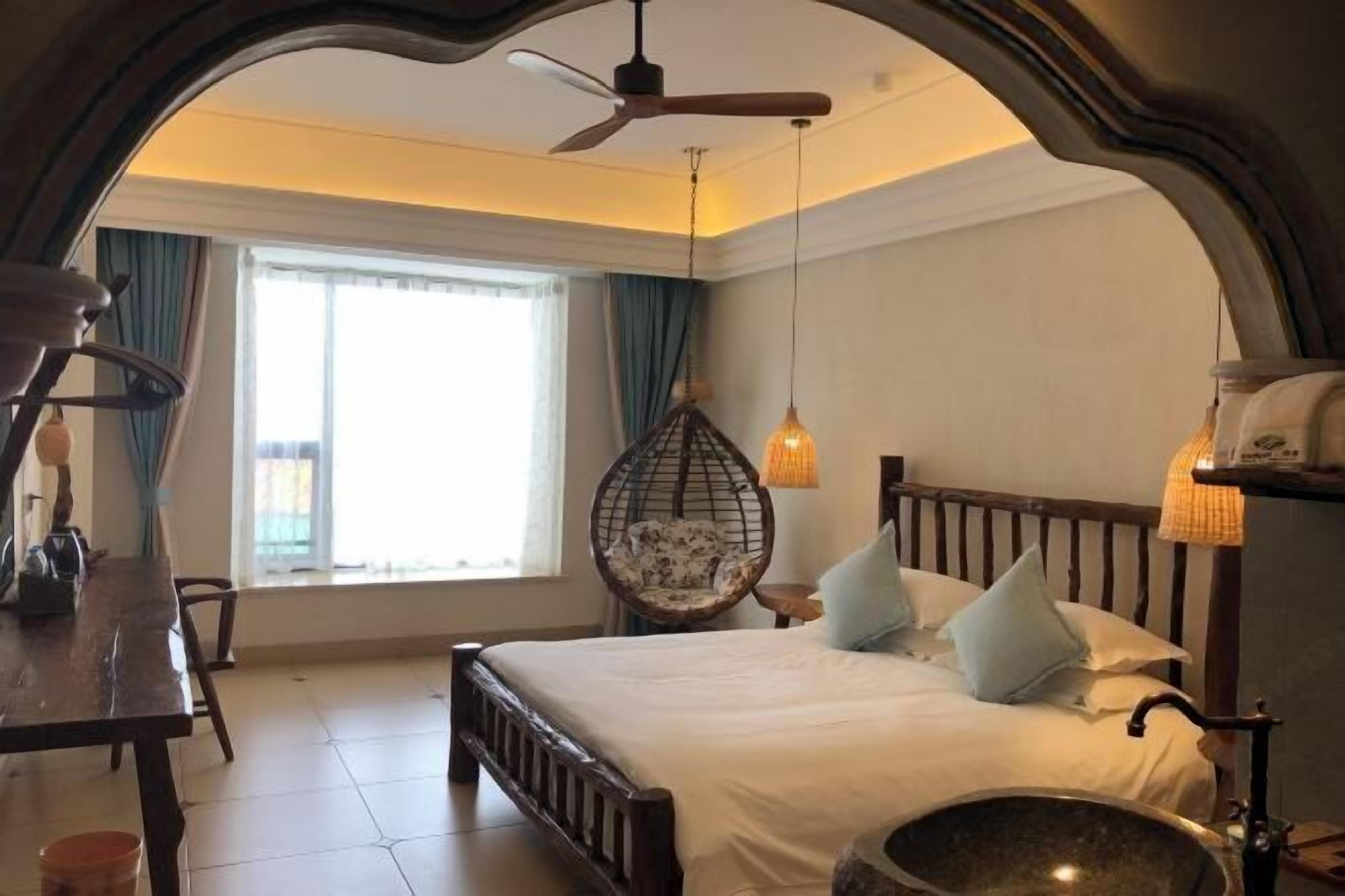 Ein Schlafzimmer mit einem hölzernen Bett, einem Hängekorbsessel, einem Esstisch und einem großen Fenster mit Vorhängen.