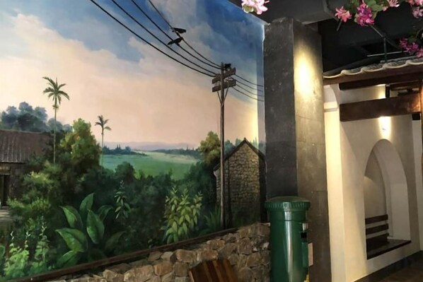 A mural of a rural landscape with a stone wall and a trash bin.