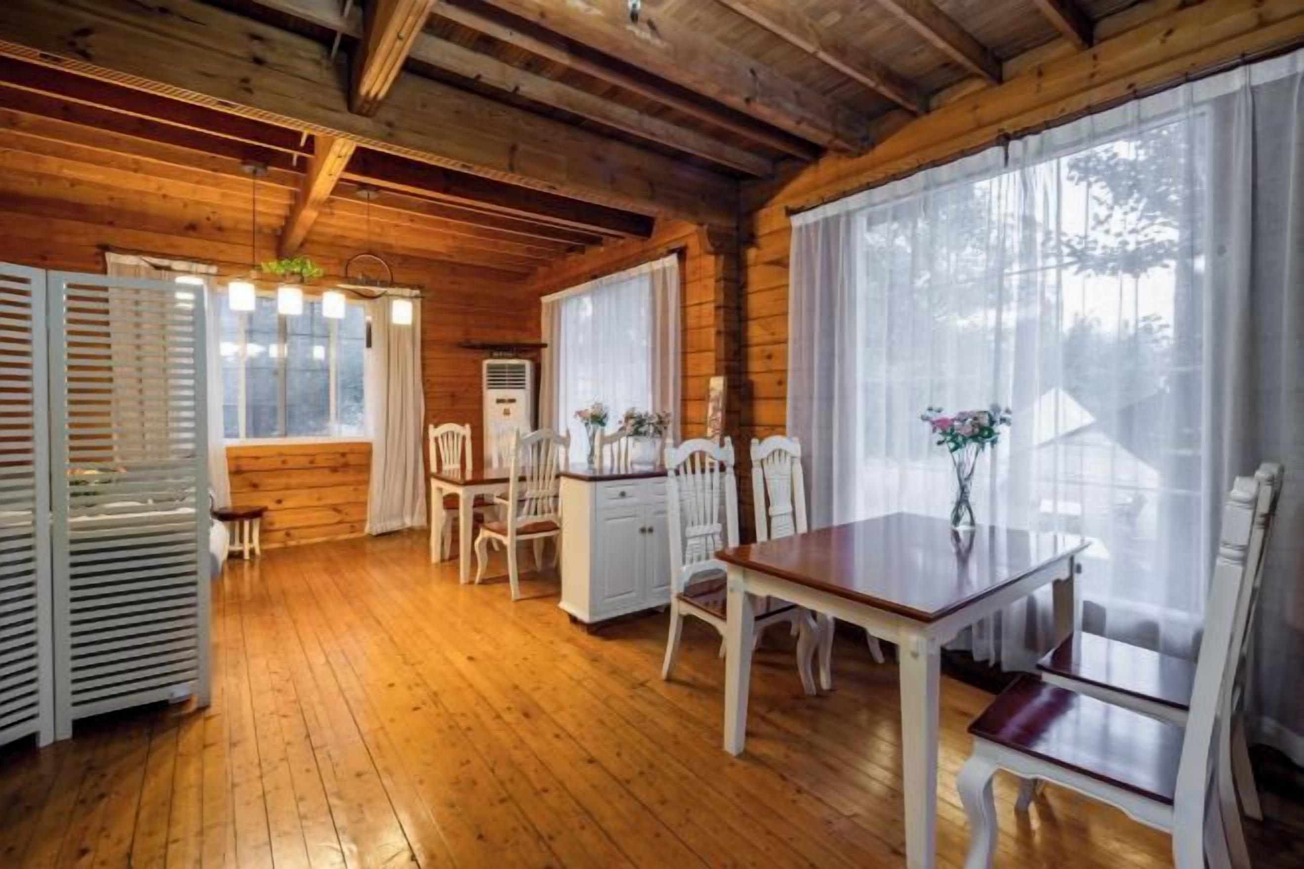 A wooden interior with a dining table, chairs, and a window with curtains.