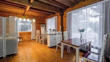 A wooden interior with a dining table, chairs, and a window with curtains.