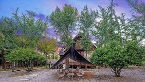 Una cabaña con fachada de madera, un comedor con mesas al aire libre y una gran estructura tipo tienda en el centro.