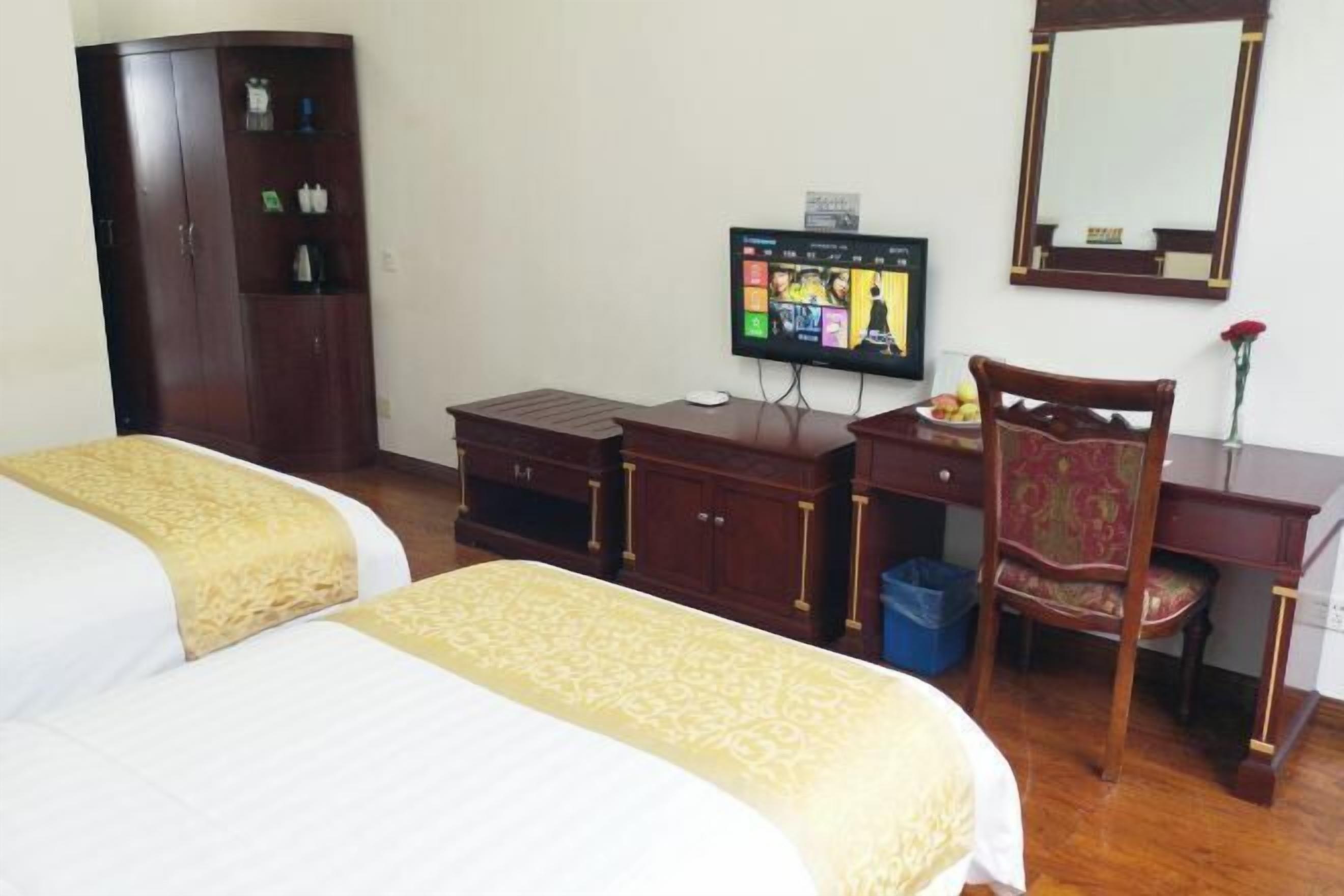 A hotel room with two beds, a desk with a computer, a television, a wardrobe, and a mirror.
