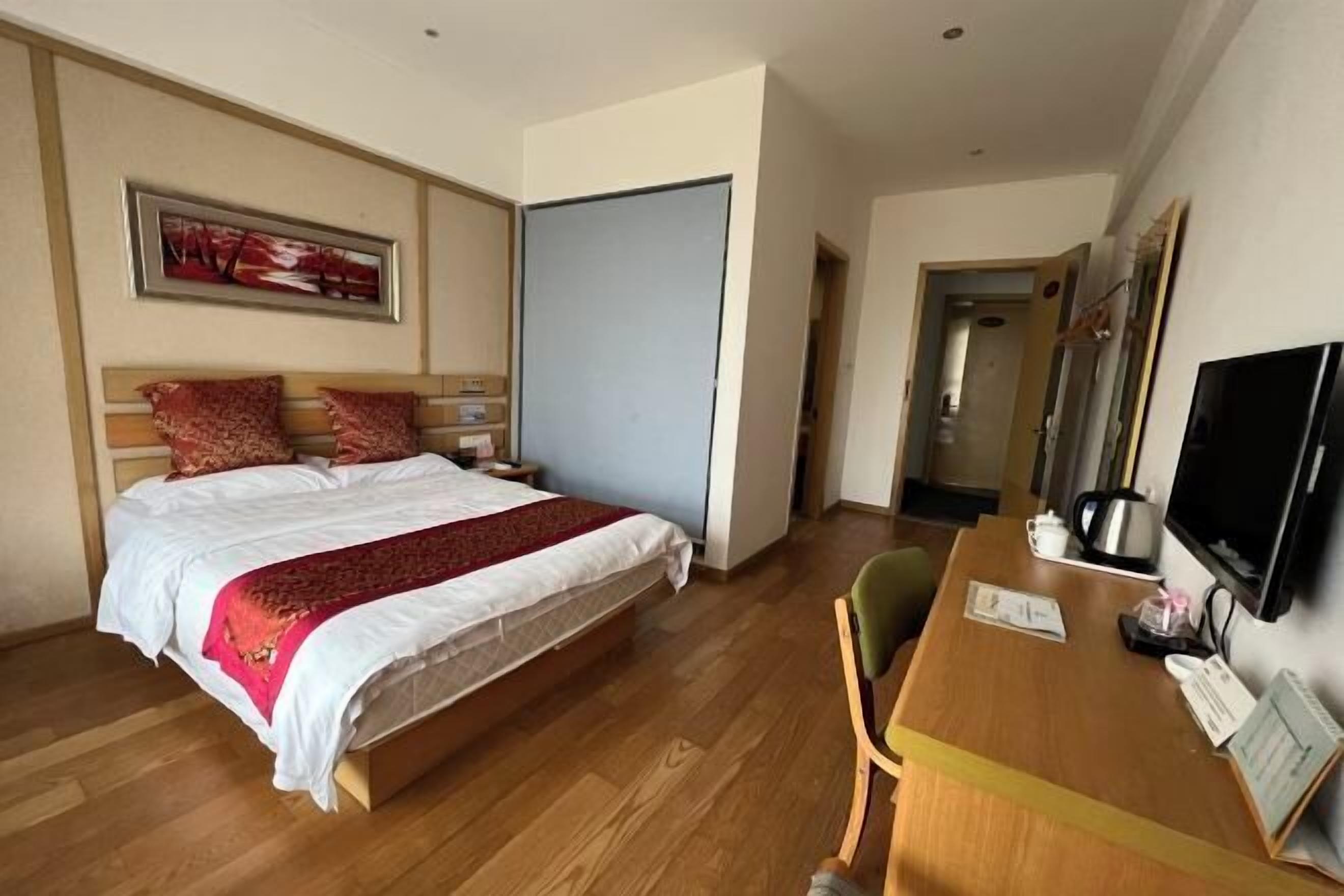 Quarto de hotel com uma cama, uma escrivaninha, uma cadeira, uma televisão e uma porta.