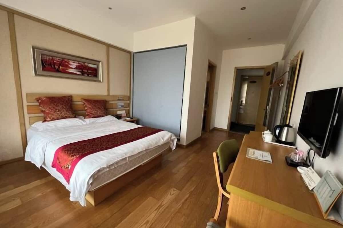 Una habitación de hotel con cama, escritorio, silla, televisor y puerta.