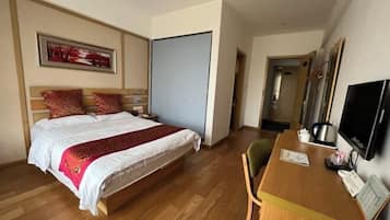 A hotel room with a bed, a desk, a chair, a television, and a door.