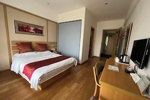 Una habitación de hotel con cama, escritorio, silla, televisor y puerta.