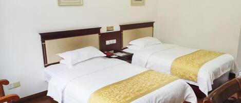 Una habitación de hotel con dos camas individuales, cabeceros de madera, ropa de cama blanca y suelo de madera.