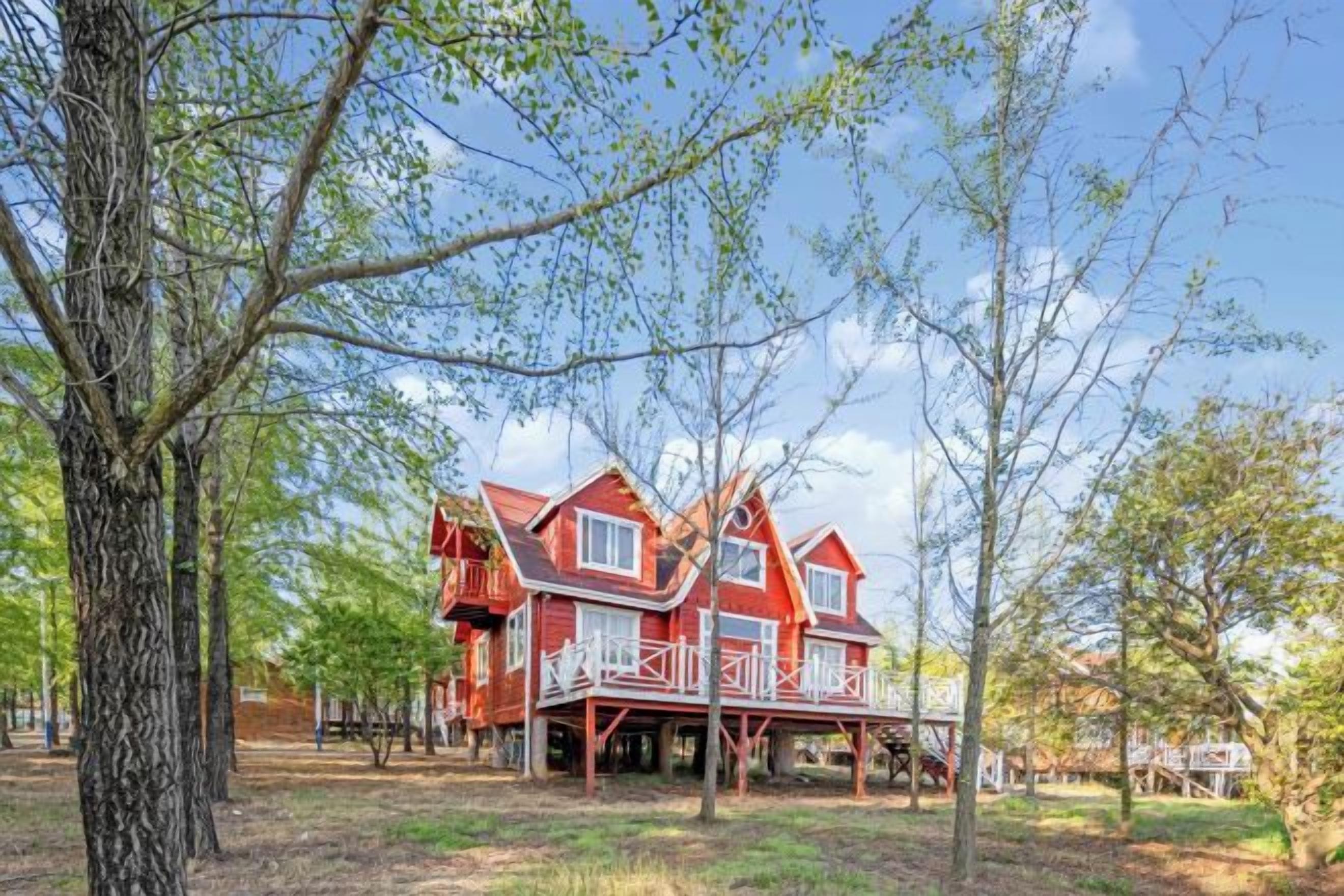 Uma casa avermelhada de vários andares com varanda, cercada por árvores.