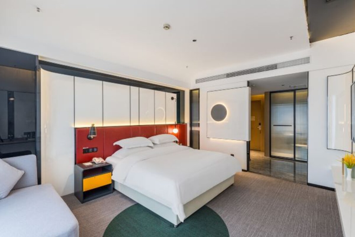 A modern hotel room with a large bed, a bedside table, a nightstand, and a mirror.