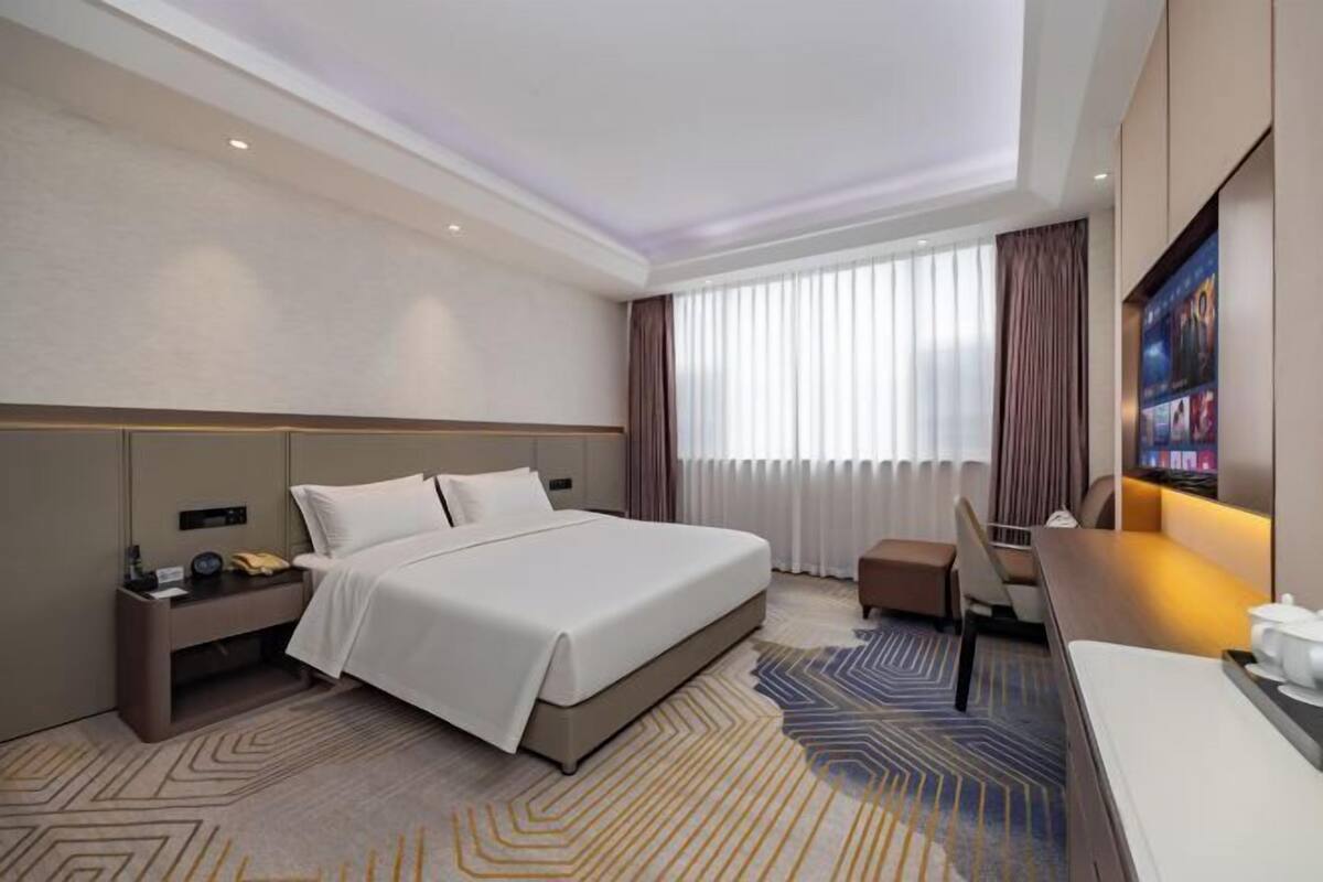 A hotel room with a large bed, bedside table, desk, and a television.