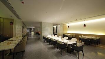 A hotel dining area with multiple tables and chairs, a long counter, and a bright overhead light.