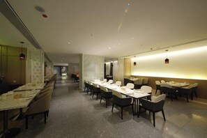 Un comedor de hotel con varias mesas y sillas, una barra alargada y una luz brillante en el techo.