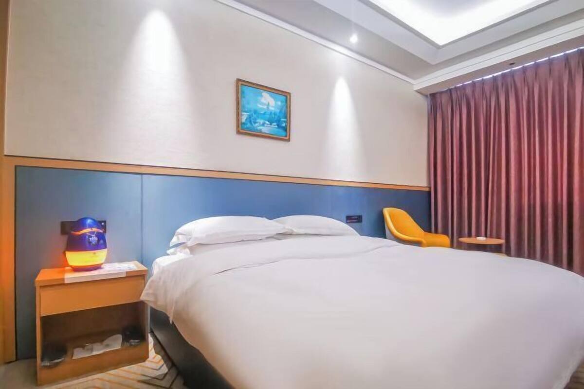 A hotel room with a bed, a nightstand with a lamp, a chair, a small table, and a picture on the wall.