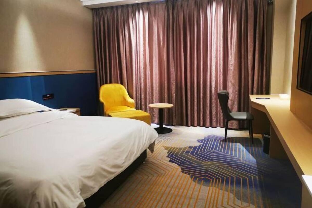 A hotel room with a bed, a desk, a chair, a small table, and a curtain.