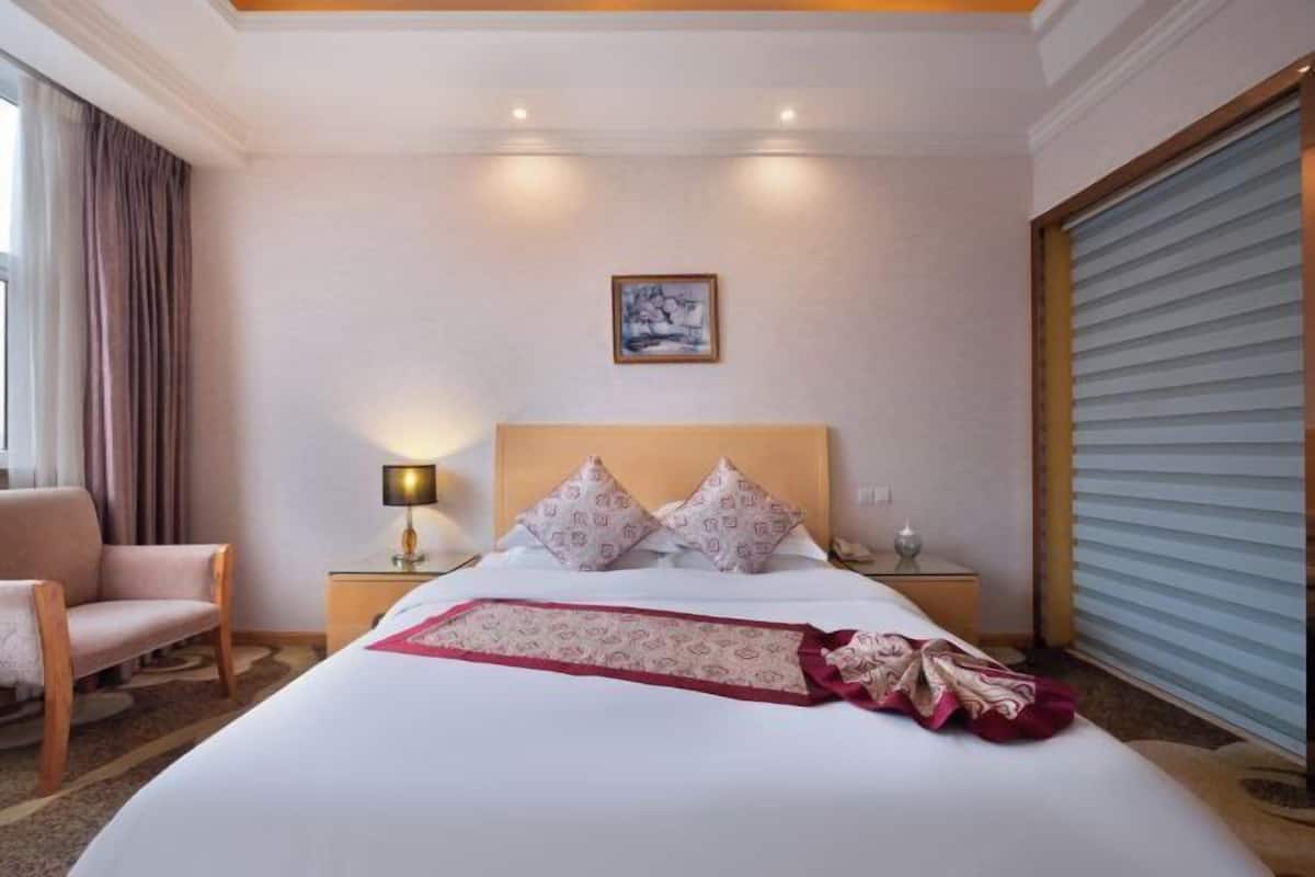 A hotel room with a large bed, a nightstand, a lamp, a chair, and a window with curtains.