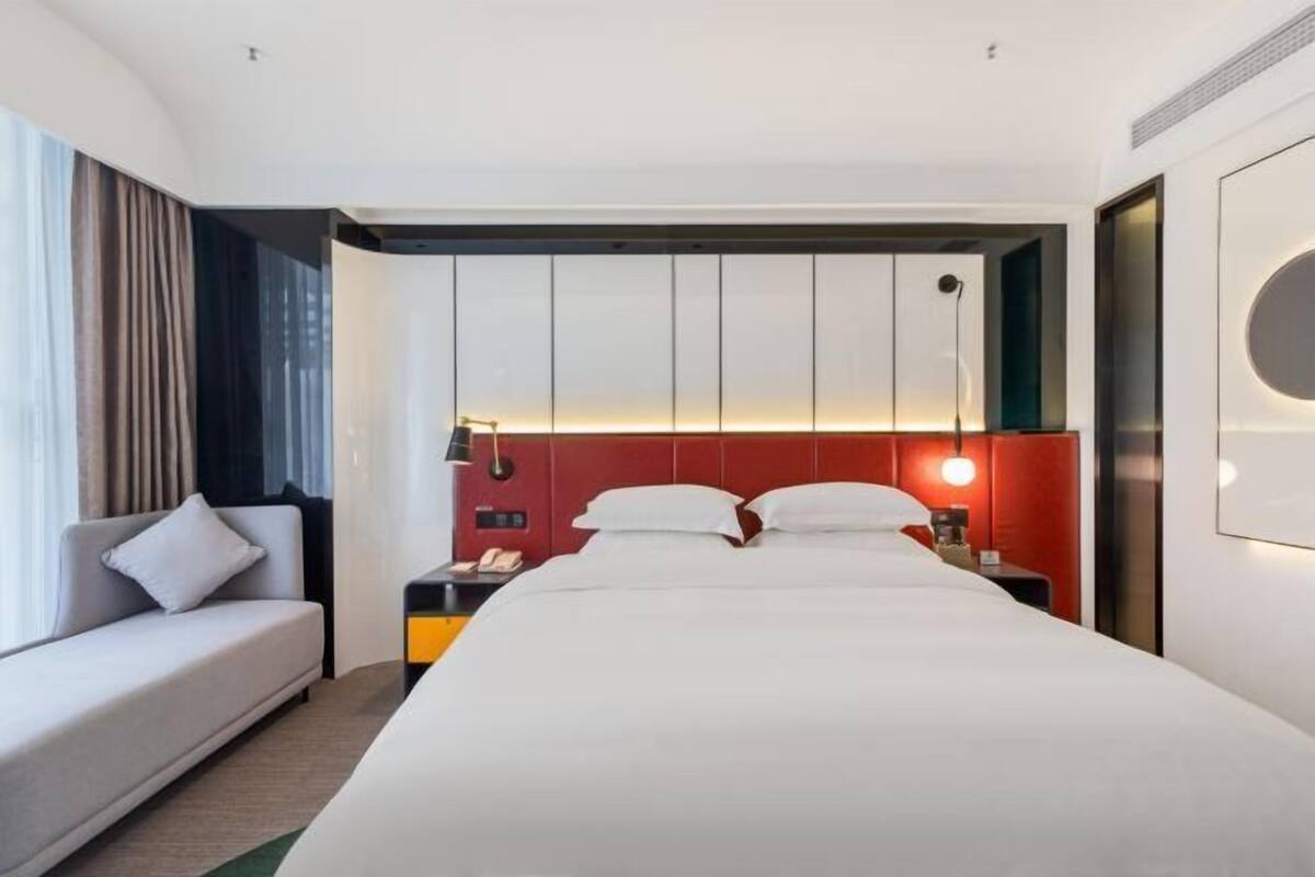 A hotel room with a large bed, a sofa, a nightstand, and a wall-mounted lamp.