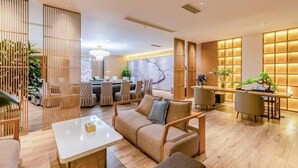 A modern hotel lobby with a wooden reception desk, a seating area with sofas and chairs, and a dining area with tables and chairs. - Tian Bo Hotel (Qianwei County)