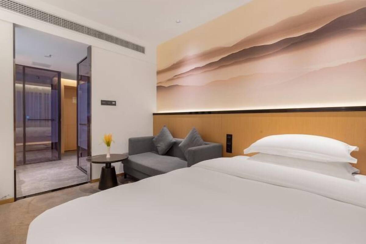 A hotel room with a bed, a sofa, a small table, and a painting on the wall.