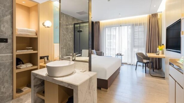 A modern hotel room with a large bed, a bathroom with a large mirror, a desk, and a TV. - Tian Bo Hotel (Qianwei County)