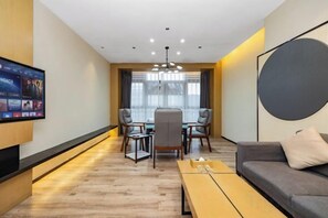Habitación de hotel moderna con televisor de pantalla plana, una mesa de comedor con sillas, un sofá y una gran pared circular decorativa.