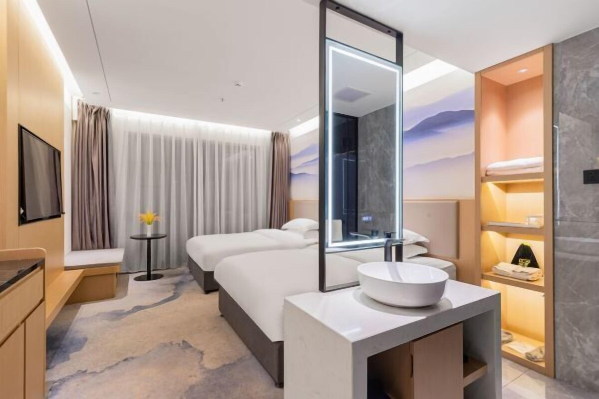 A modern hotel room with a large bed, a bedside table, a round mirror, and a built-in sink.