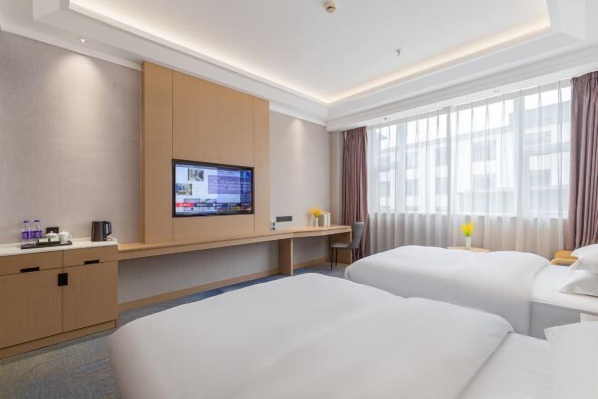 A hotel room with a bed, a desk, a TV, and a window with curtains.