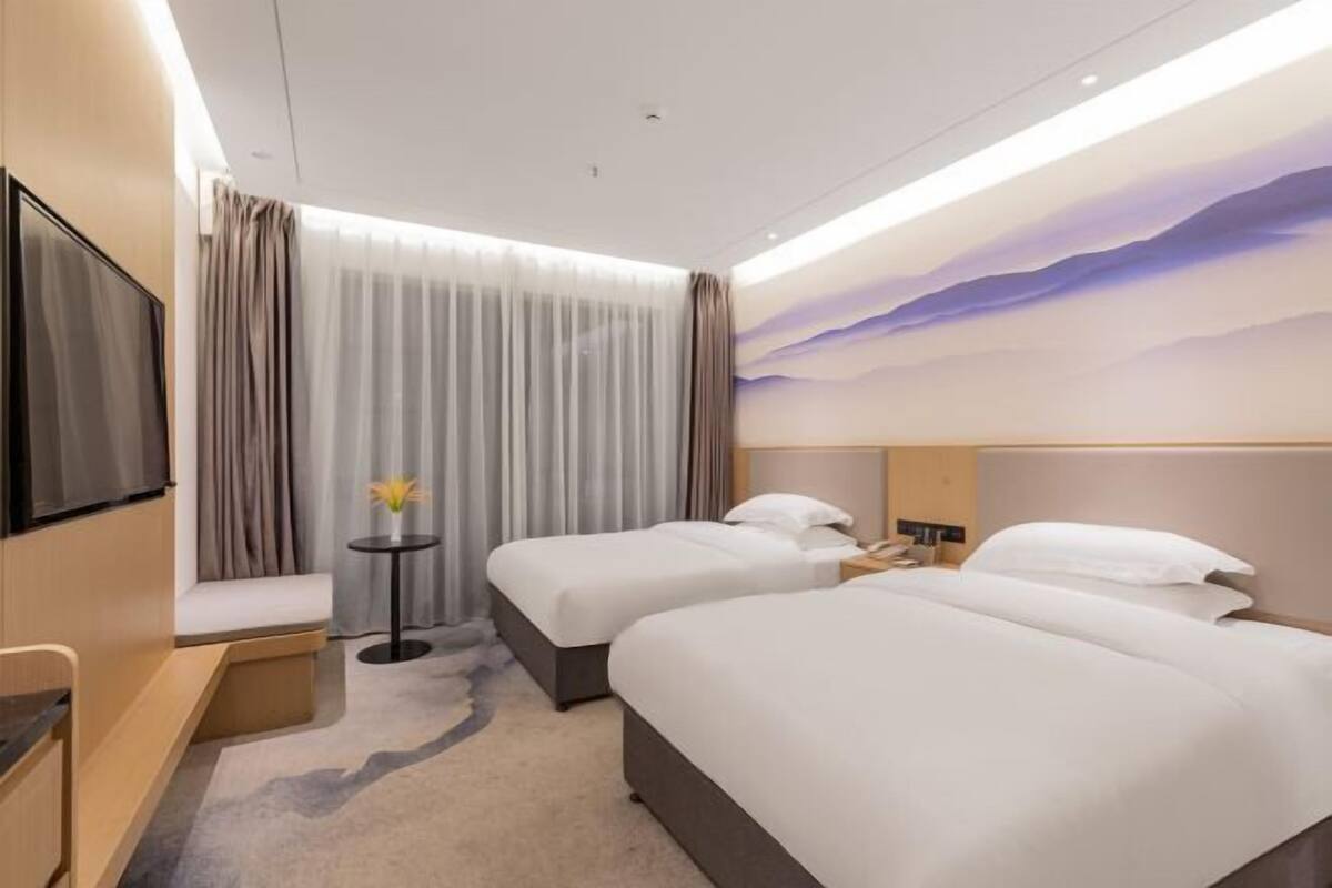 A hotel room with two beds, a TV, a small table with a vase, and a painting on the wall.