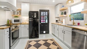 A modern kitchen with white cabinetry, a black refrigerator, stainless steel appliances, and a checkered rug. - 1 King and 1 Queen - Close to just about Everything (Fredericksburg)