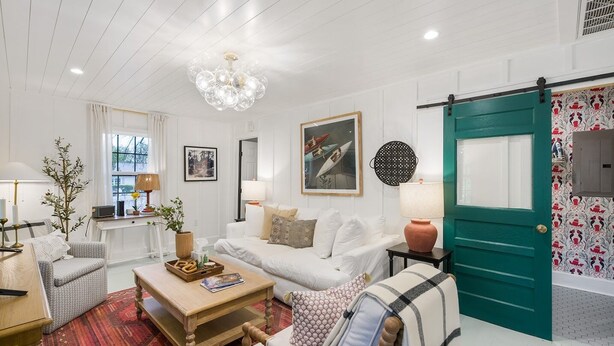 A modern living room with a white sofa, a wooden coffee table, and a red patterned rug. There is a green door and a wall with a decorative pattern. - 1 King and 1 Queen - Close to just about Everything (Fredericksburg)