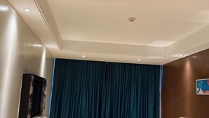 Una habitación con una cortina azul oscuro, un televisor de pantalla plana montado en la pared e iluminación empotrada en el techo.