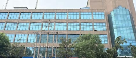 A multi-story building with a modern glass facade, several storefronts with signage, and a clear sky.