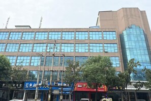 Ein mehrstöckiges Gebäude mit moderner Glasfassade, mehreren Geschäften mit Beschilderung und blauem Himmel.