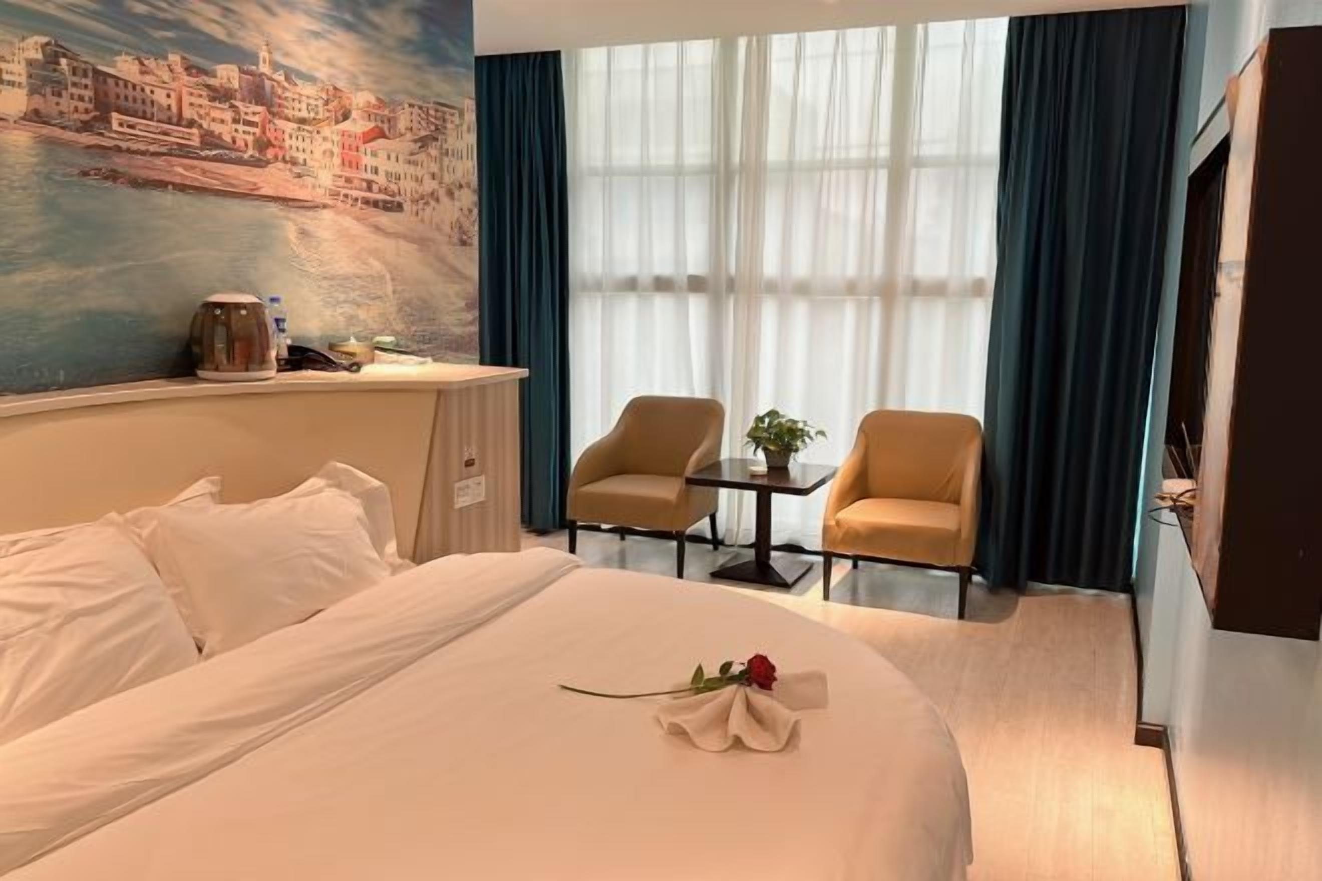 Ein Hotelzimmer mit einem Bett, einem Schreibtisch, zwei Stühlen, einem fenster mit Vorhängen und einem Bild an der Wand.