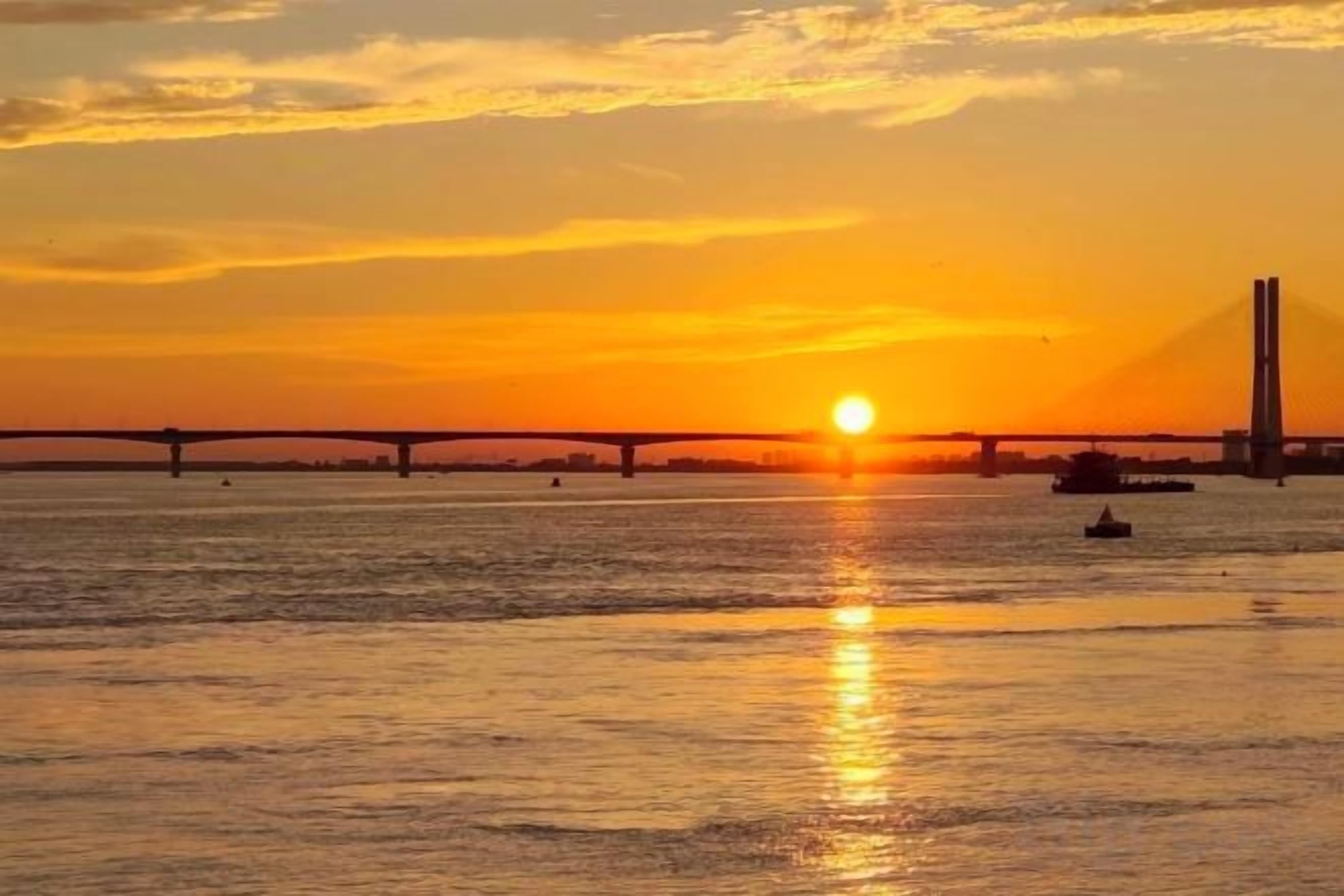 Un atardecer sobre un cuerpo de agua con un puente al fondo.
