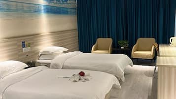 Ein Hotelzimmer mit zwei Betten, einem Schreibtisch, zwei Stühlen, einem Nachttisch und einem Wandbild mit einer Strandansicht.