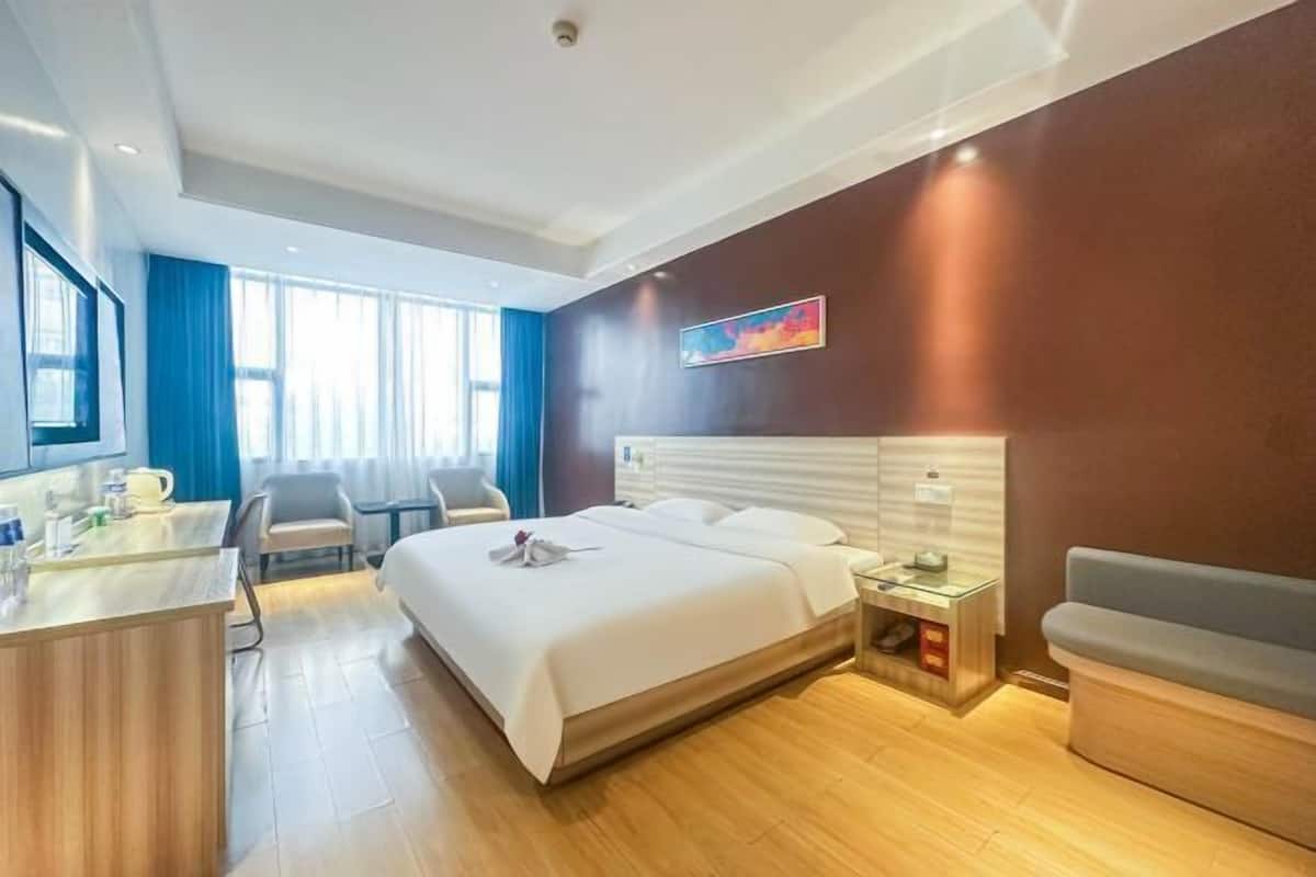 Una habitación de hotel con cama, mesita de noche, silla, escritorio y ventana con cortinas.