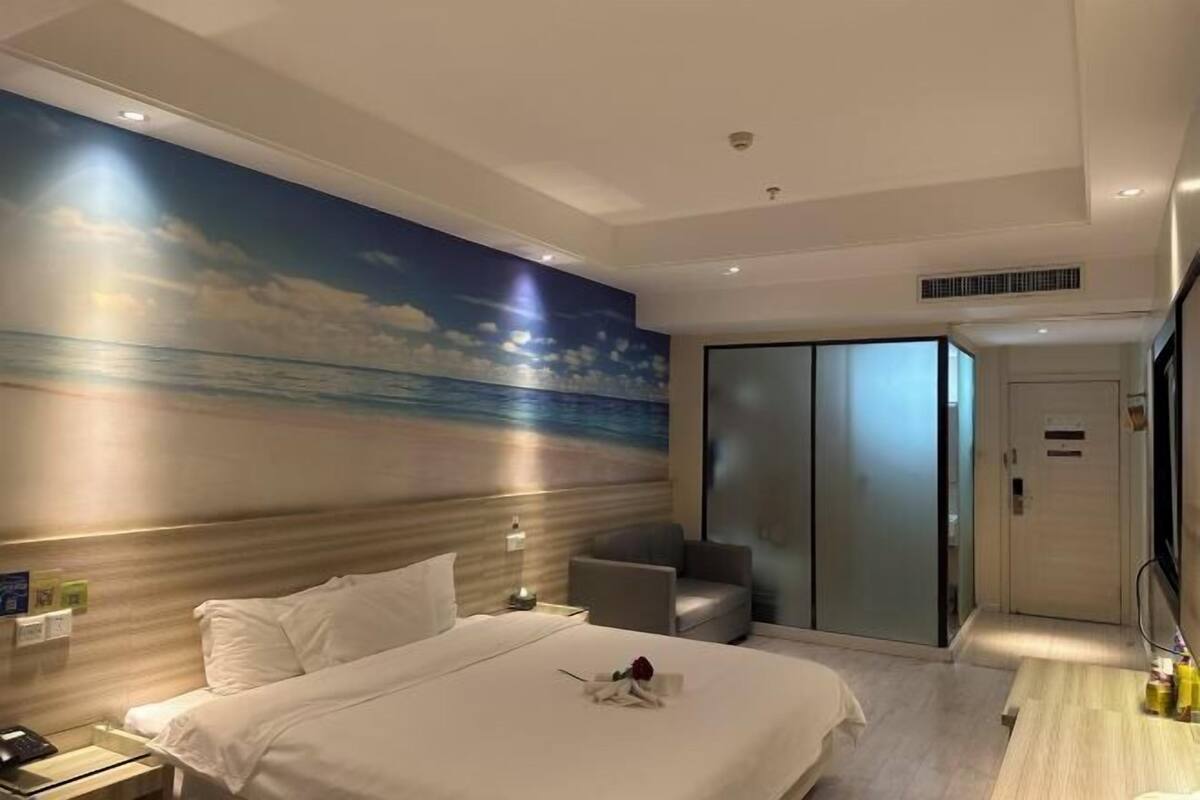 Habitación de hotel con cama, mesita de noche, escritorio, silla, armario y un mural de una escena de playa.