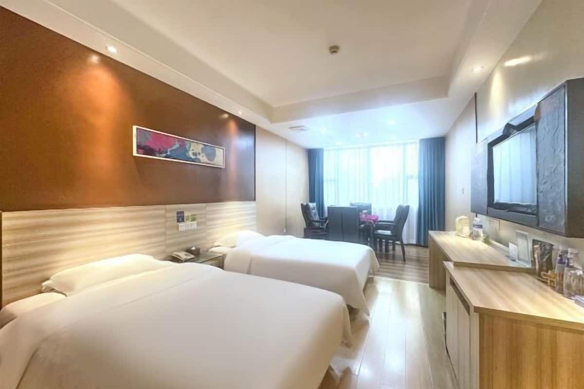 Una habitación de hotel con dos camas, un escritorio, una silla, un televisor y un cuadro en la pared.