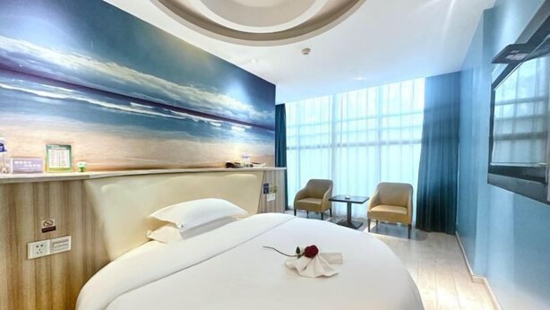 Habitación de hotel con cama, escritorio, dos sillas, un ventanal grande y un mural en la pared.