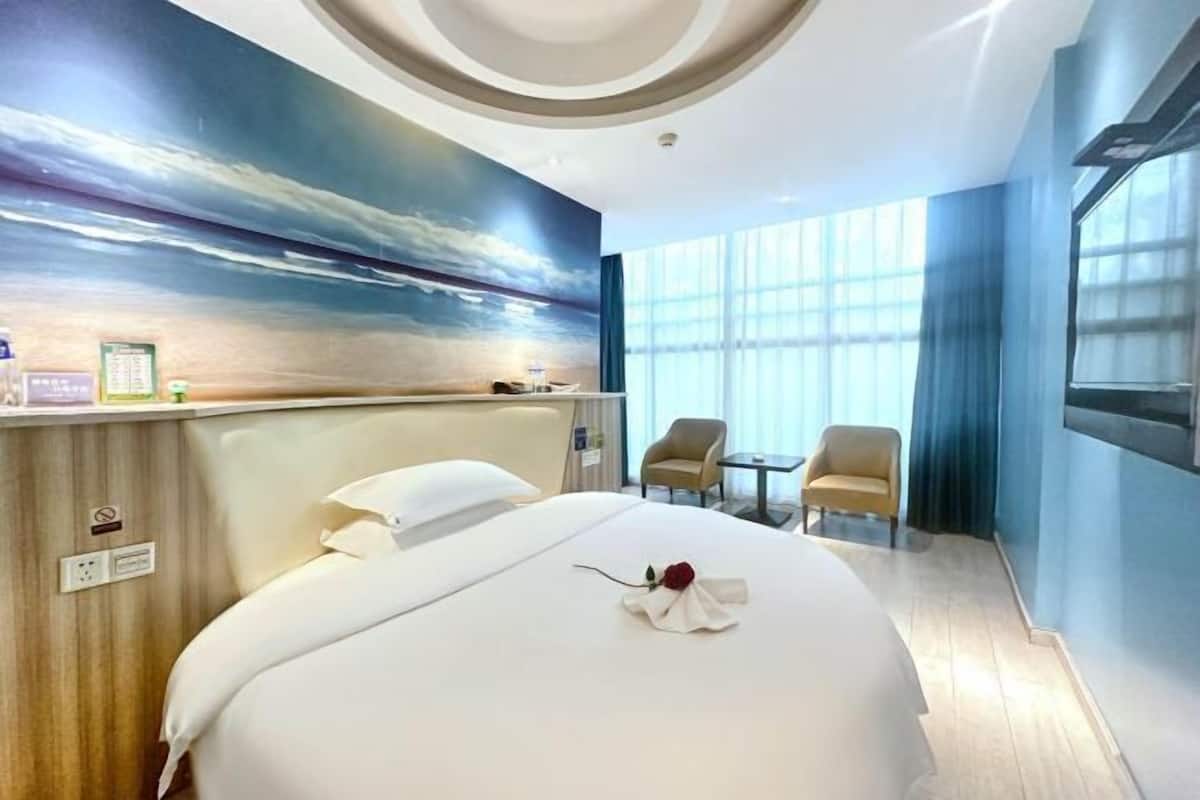 Habitación de hotel con cama, escritorio, dos sillas, un ventanal grande y un mural en la pared.