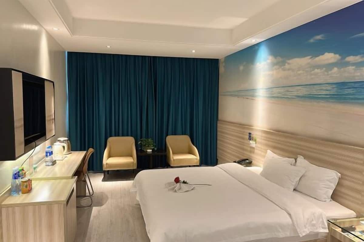 Habitación de hotel con cama, escritorio, dos sillas, televisión y una ventana grande con vista a la playa.