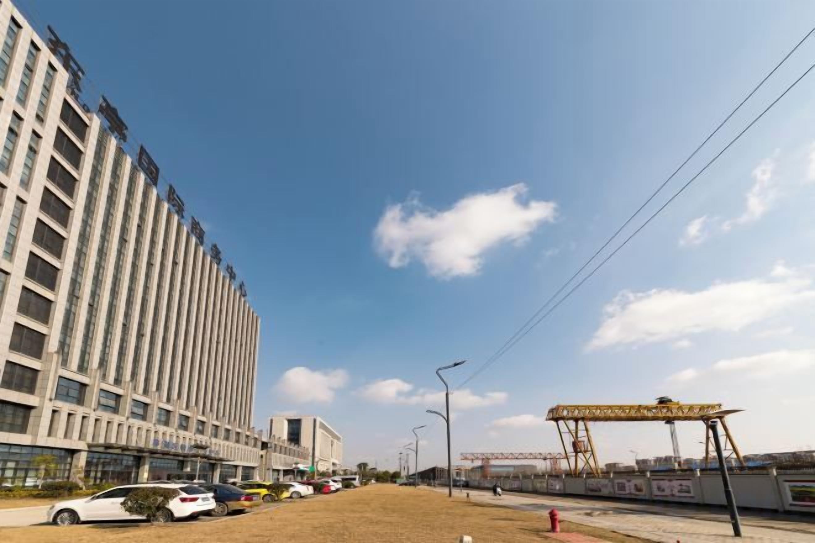 A modern building with a flat facade, a parking lot with several cars, and a clear sky.
