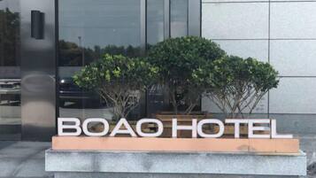 Un letrero para BOAO HOTEL con un diseño moderno, que muestra una vista clara de la fachada del edificio y un área ajardinada con arbustos.